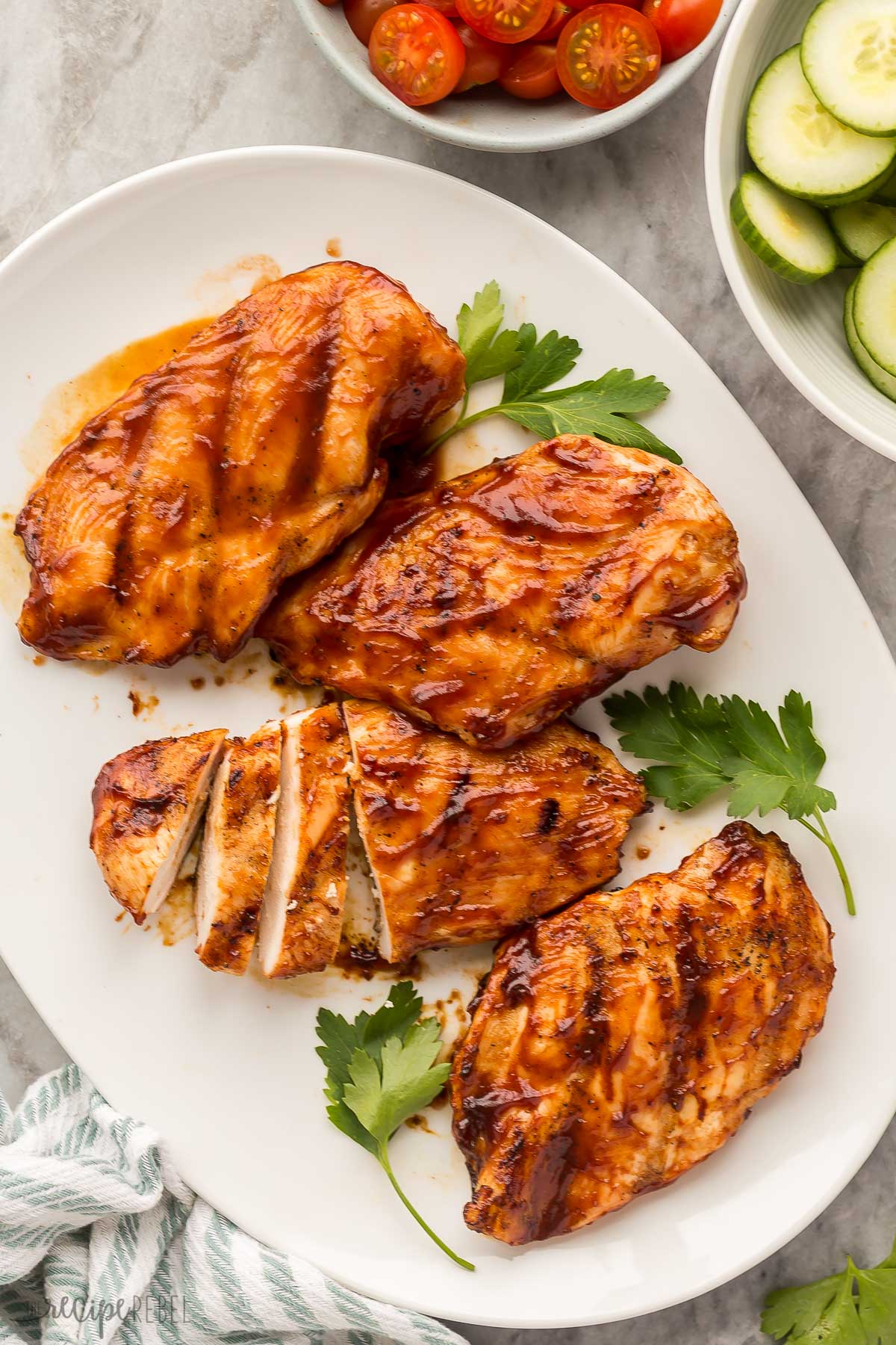 overhead image of four bbq chicken breasts with vegetables on the side