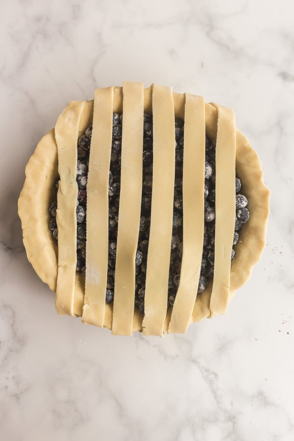 overhead image of blueberry pie crust with pie crust strips in one direction