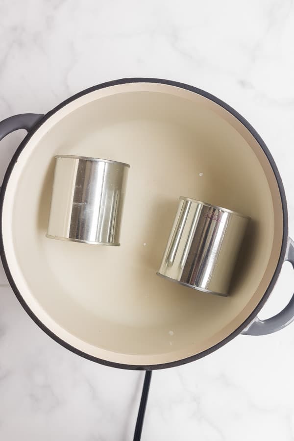 two cans of sweetened condensed milk in pot of water