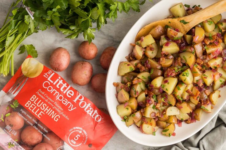 This German Potato Salad is made with red potatoes, bacon, and a homemade dressing made of sauteed onion, vinegar, bacon drippings.. Serve it warm or chilled! #salad #potatoes #recipes | easy recipes | side dish recipes | little potatoes | summer recipes overhead image of german potato salad with bag of Little potatoes