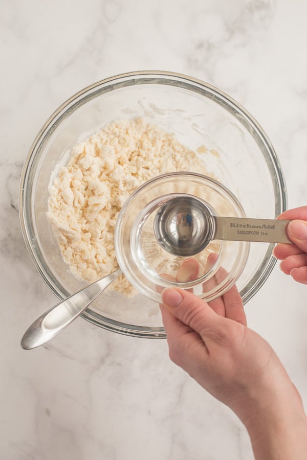tablespoon with water over top of bowl of pie crust ingredients