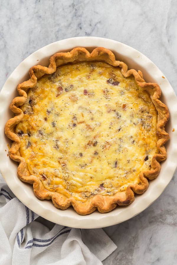 This Quiche Lorraine is a rich and flavorful quiche recipe, made with bacon, sauteed onions, cheese and a creamy egg base. It's make ahead and freezer friendly! #quiche #breakfast #brunch | breakfast recipe | brunch | mother's day | eggs | bacon overhead image of quiche lorraine on marble background