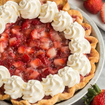 square image of strawberry pie in tin pie plate with whipped cream.