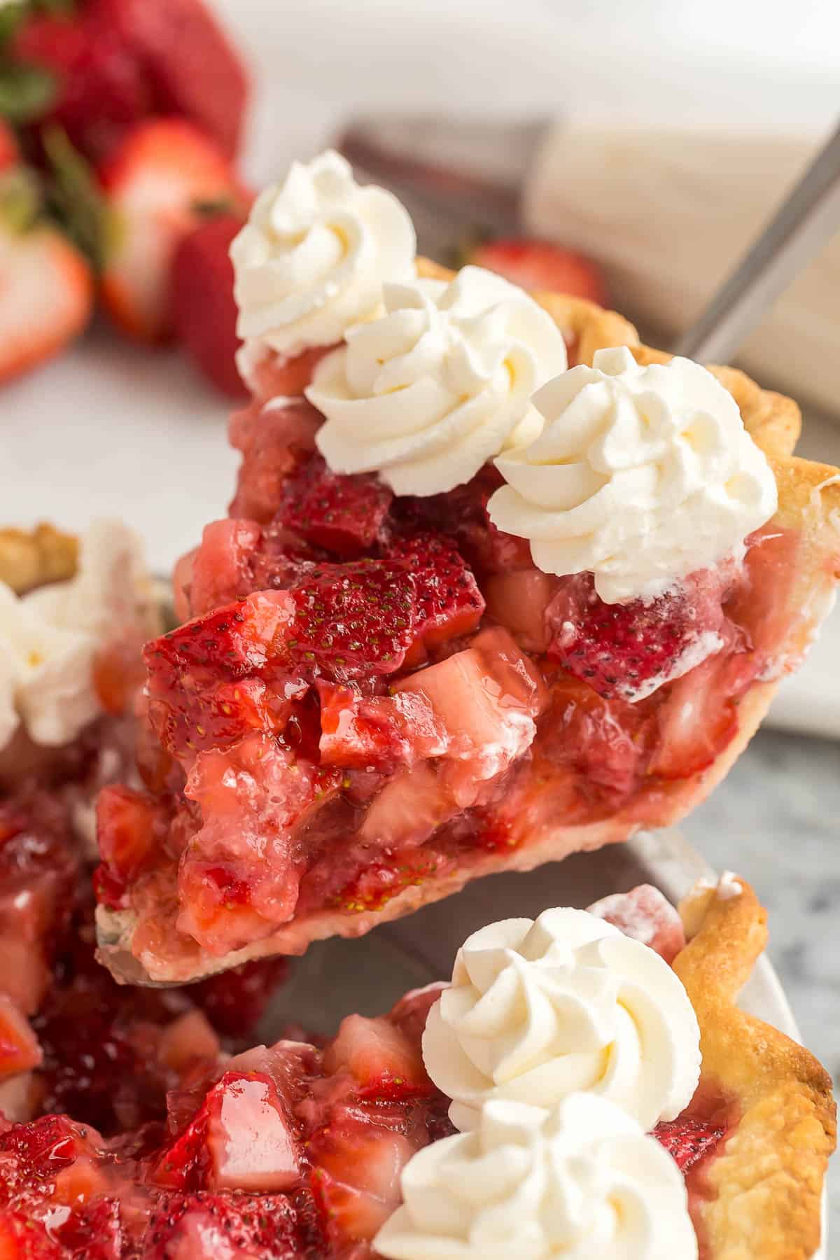 This fresh Strawberry Pie is made with real strawberries and no Jello mix in a homemade pie crust, topped with sweetened whipped cream! It's the perfect summer treat! #strawberry #dessert #recipe | dessert recipes | pie recipes | easy dessert ideas | summer dessert | strawberry recipes | summer recipes | easter pie piece of strawberry pie being lifted out of pie plate.