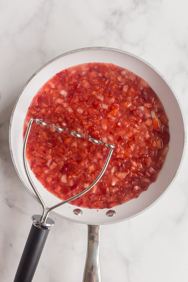 strawberries in white skillet with potato masher