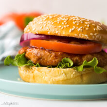 close up image of chicken burger in bun on blue plate