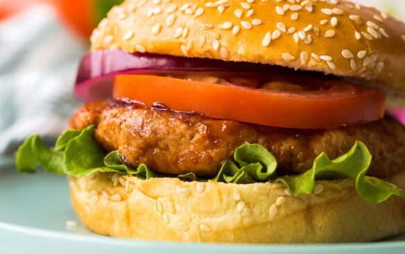 close up image of chicken burger in bun on blue plate