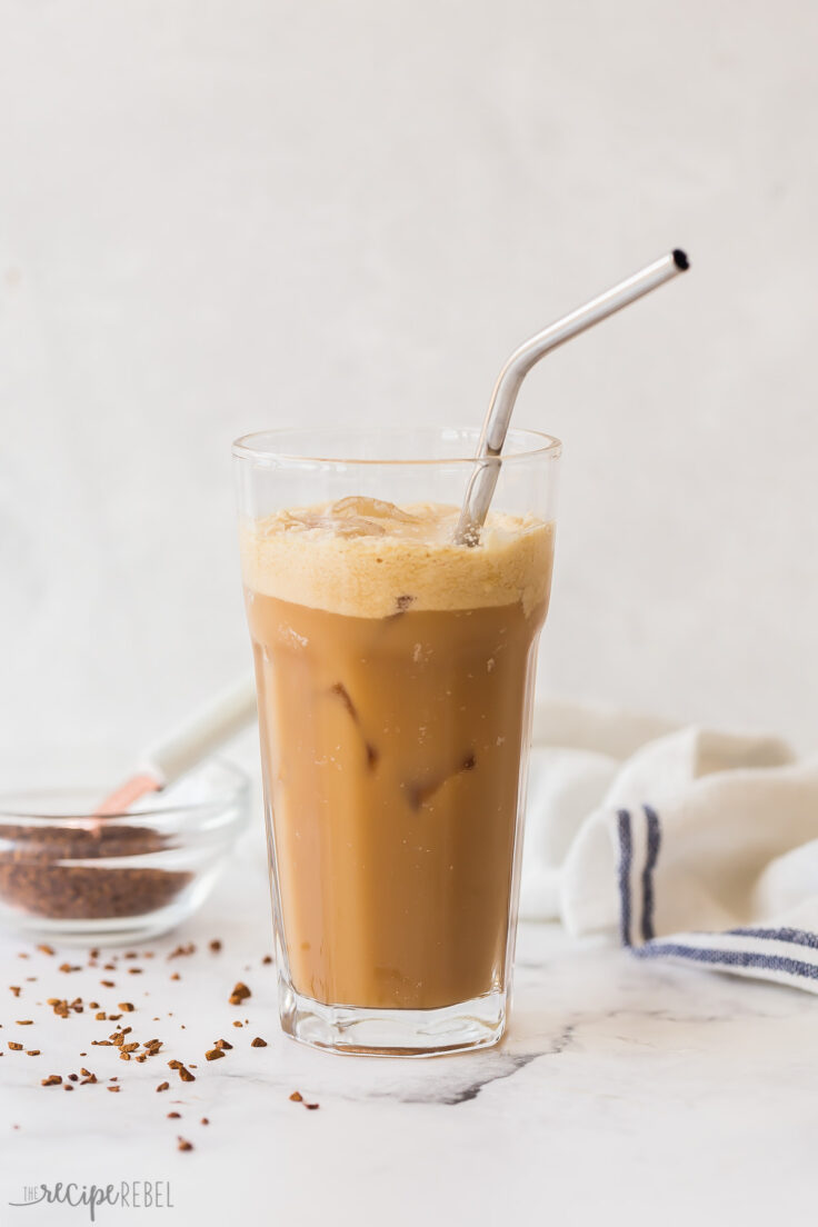 tall glass of shaken coffee frappe with instant coffee in the background