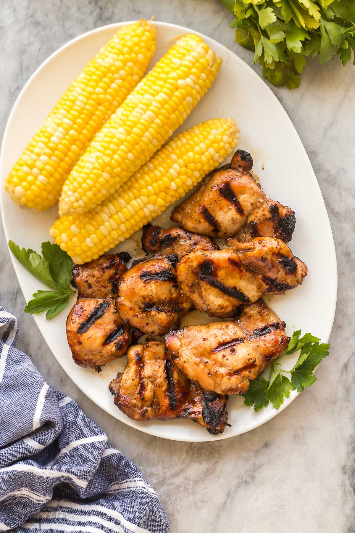overhead image of grilled chicken thighs on plate with corn on the cob