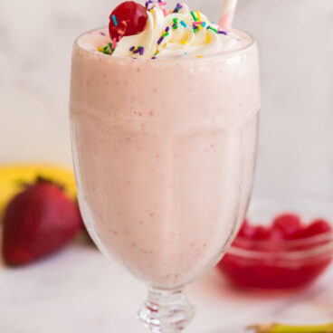 strawberry milkshake in glass with whipped cream and paper straw