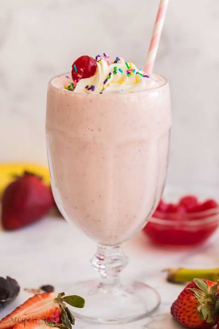 strawberry milkshake in glass with whipped cream and paper straw