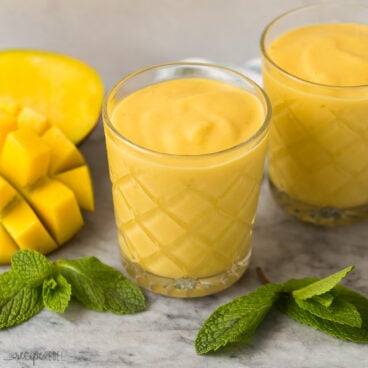 two mango smoothies in glasses with fresh mango and fresh mint