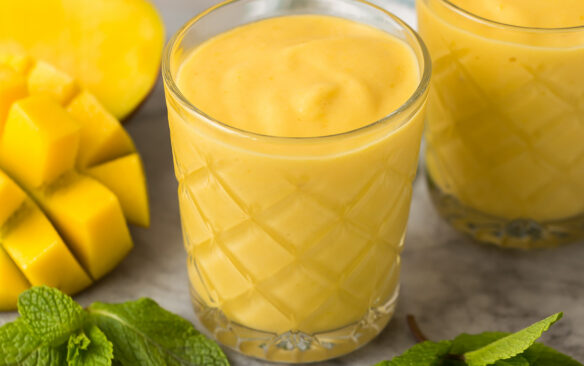 two mango smoothies in glasses with fresh mango and fresh mint