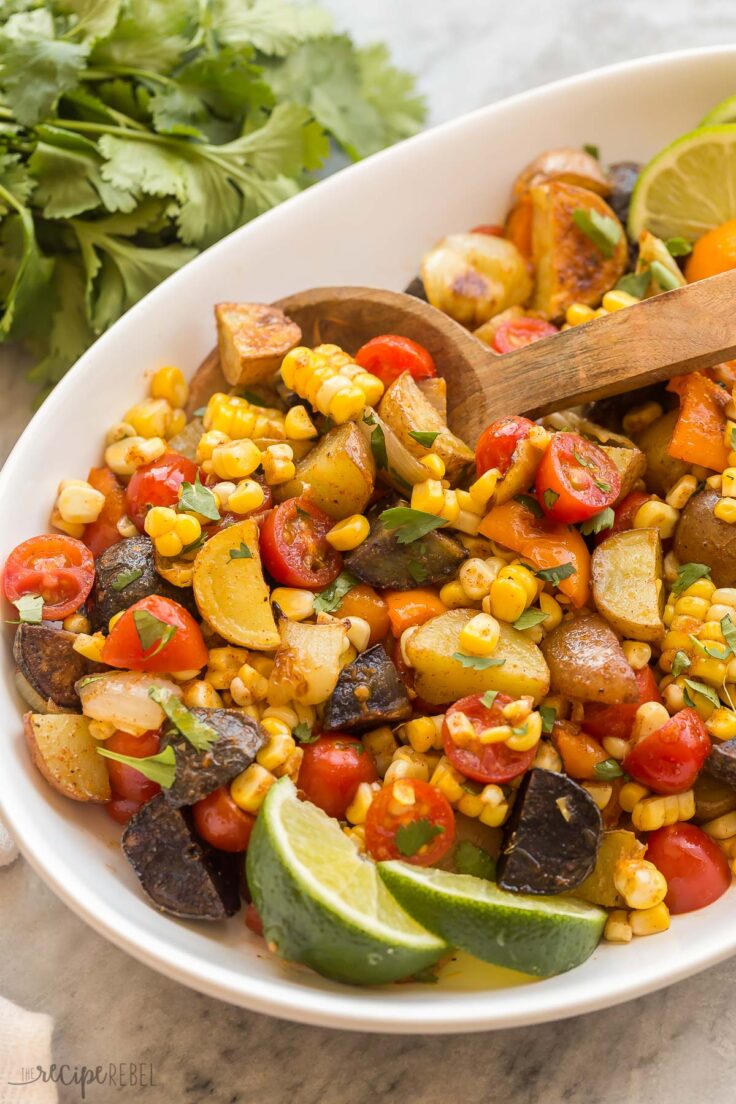 close up image of mexican potato salad with wooden spoon and lime wedges