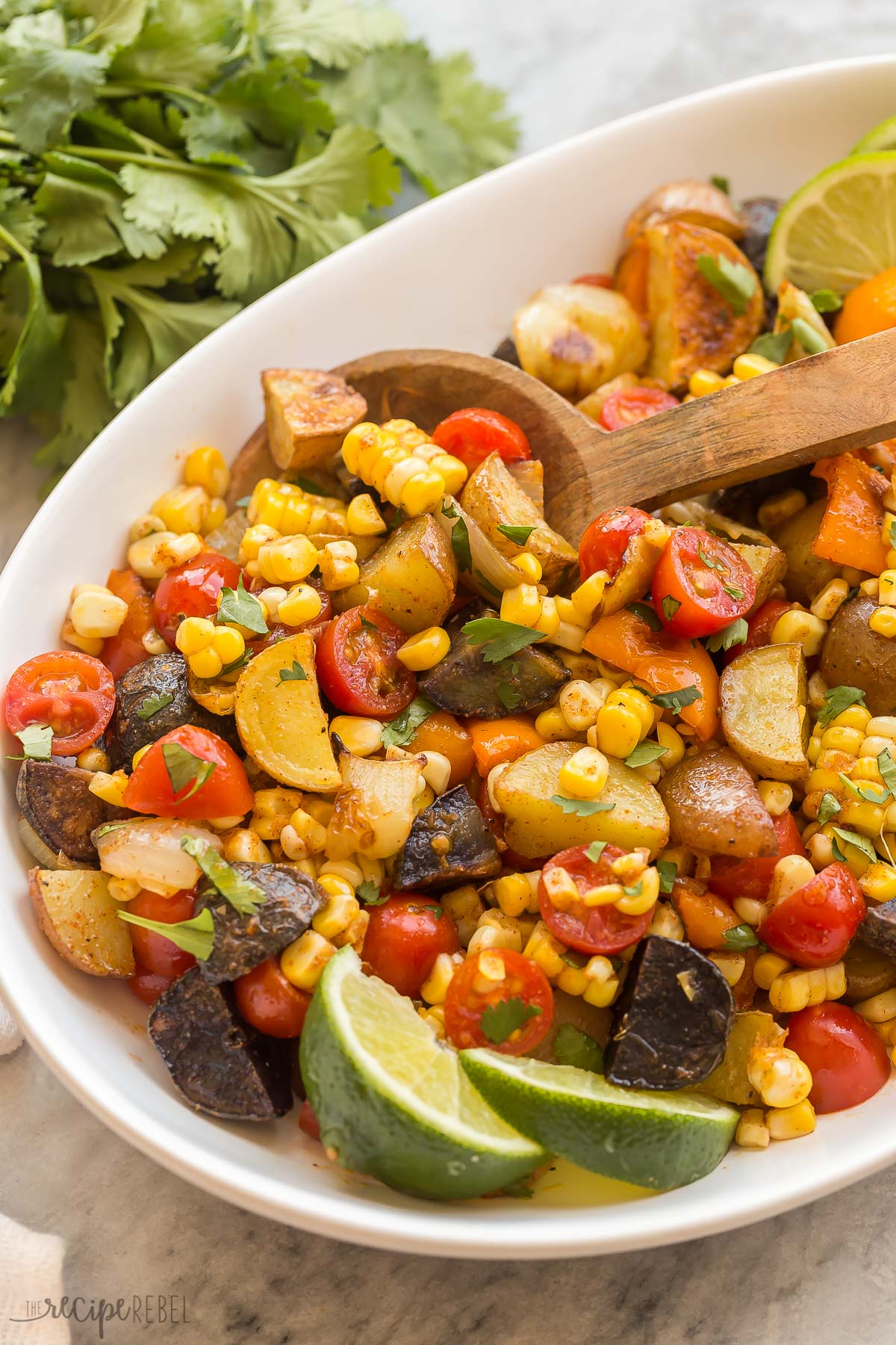 This Southwest Potato Salad is made with grilled or roasted potatoes, peppers, corn on the cob and fresh tomatoes, tossed in a taco spiced vinaigrette! #potatoes #salad #recipes | cold salad | barbecue recipes | side dish close up image of mexican potato salad with wooden spoon and lime wedges
