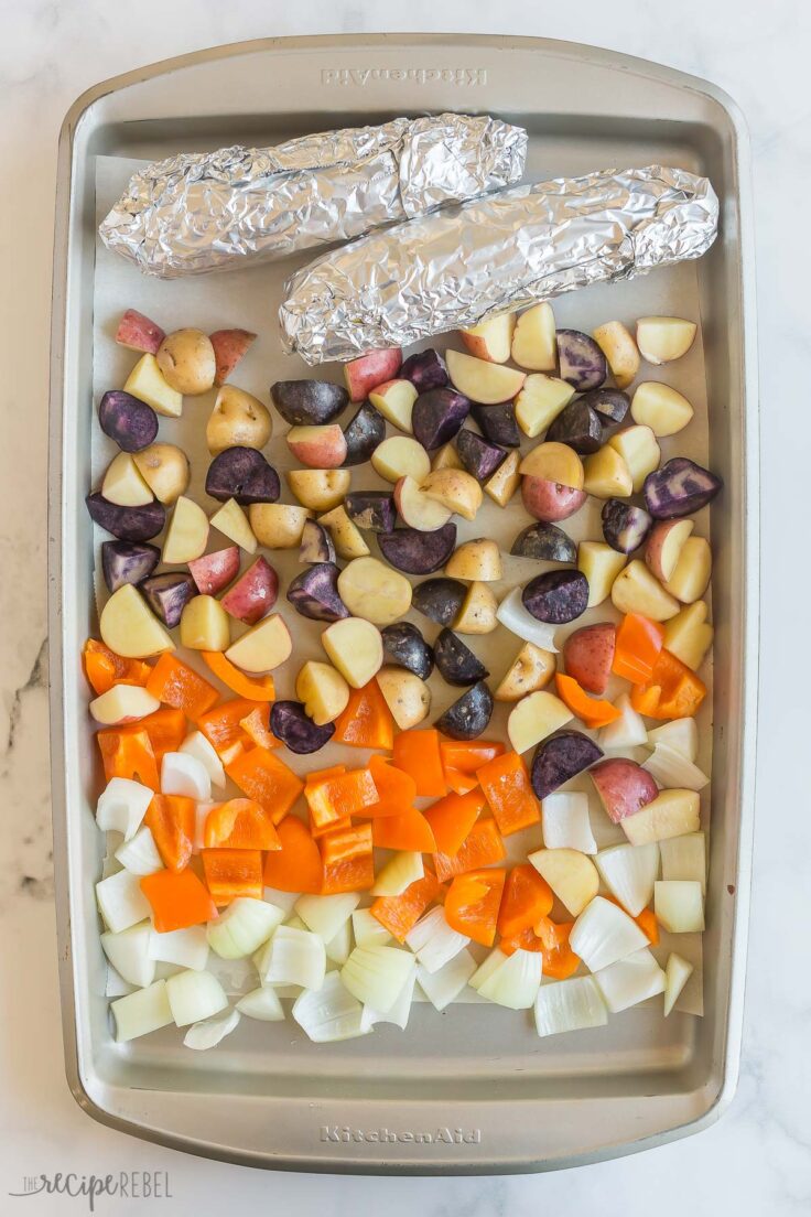 corn wrapped in foil and other vegetables on sheet pan for roasting