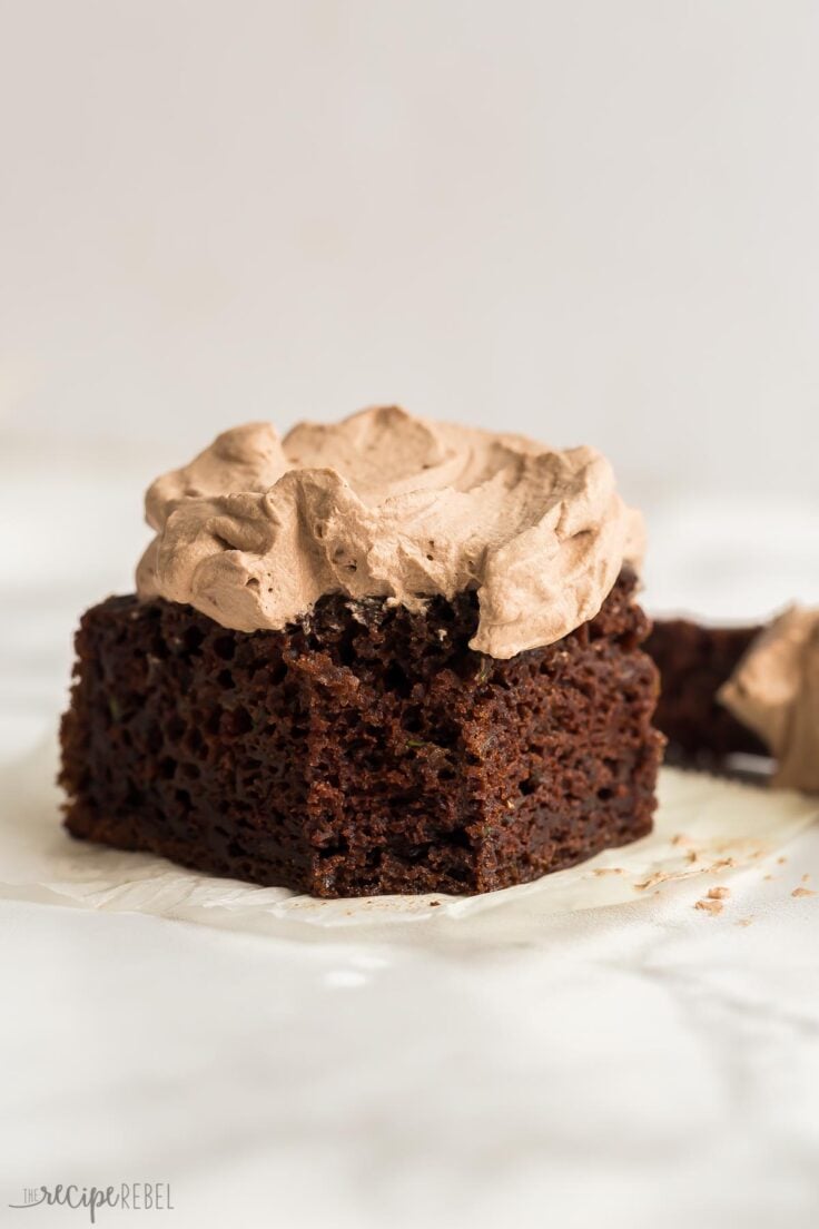 This is the BEST Chocolate Zucchini Cake! Perfectly moist, rich and fudgy and loaded with zucchini (but you'd never know)! Topped with chocolate whipped cream. #chocolate #dessert | zucchini cake | zucchini recipes | chocolate cake | best chocolate cake square piece of zucchini cake with one bite missing