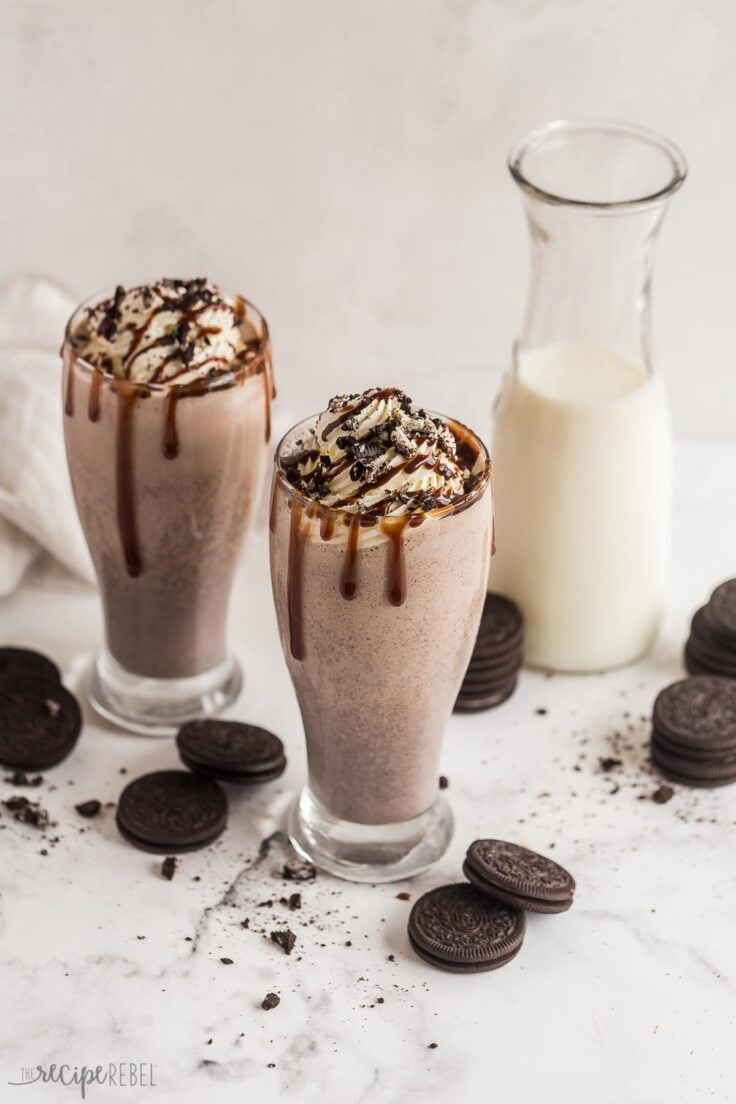 two oreo milkshakes in glasses with milk in the background