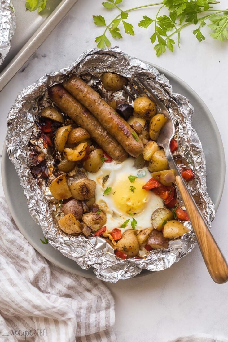 Breakfast Foil Packs are an easy camping meal, loaded with breakfast potatoes, sausage and eggs. Great on the grill, over the fire, or in the oven! #breakfast #grilling #camping | camping recipes | camping meals | foil packets | camping breakfast overhead image of breakfast foil pack on plate with fork