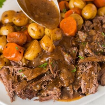 square image of slow cooker pot roast with gravy being drizzled over.