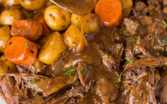 square image of slow cooker pot roast with gravy being drizzled over.