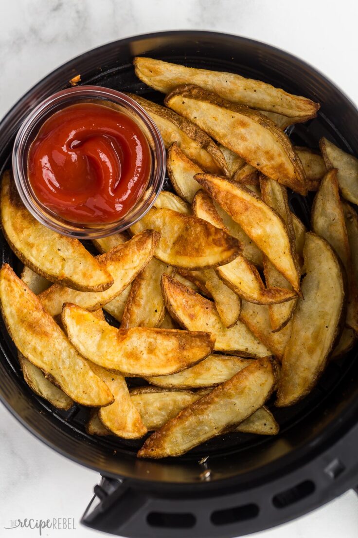 close up image of potato wedges in air fryer basket with ketchup