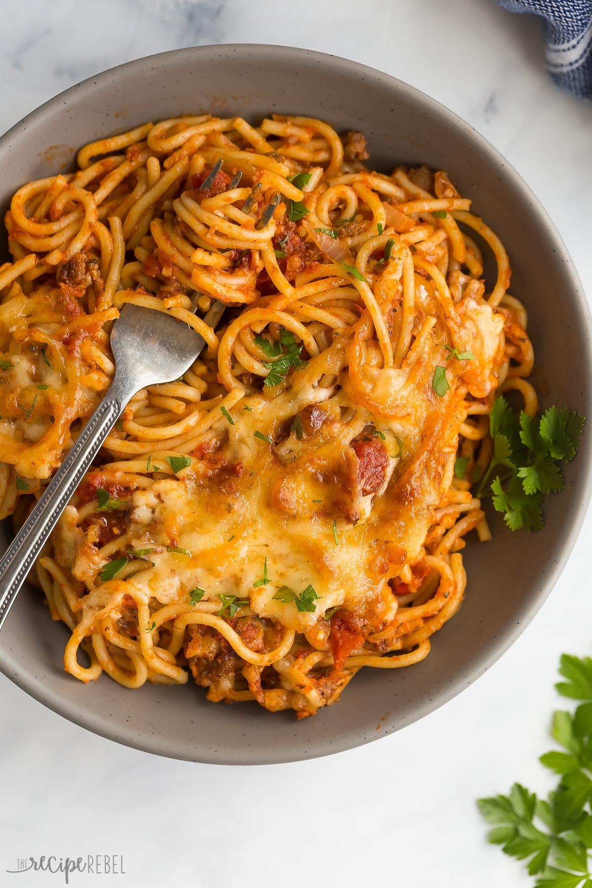 This easy Baked Spaghetti is made with a homemade Italian sausage spaghetti sauce, cooked spaghetti and loads of cheese! It's a make ahead and freezer friendly weeknight dinner that the whole family loves. #dinner #recipe #pasta | spaghetti recipe | dinner ideas | comfort food | meal prep | make ahead meals | pasta bake | casserole recipe spaghetti in grey bowl with fork stuck in noodles