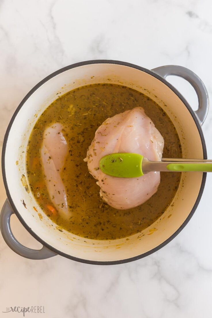 raw chicken breasts being added to soup pot