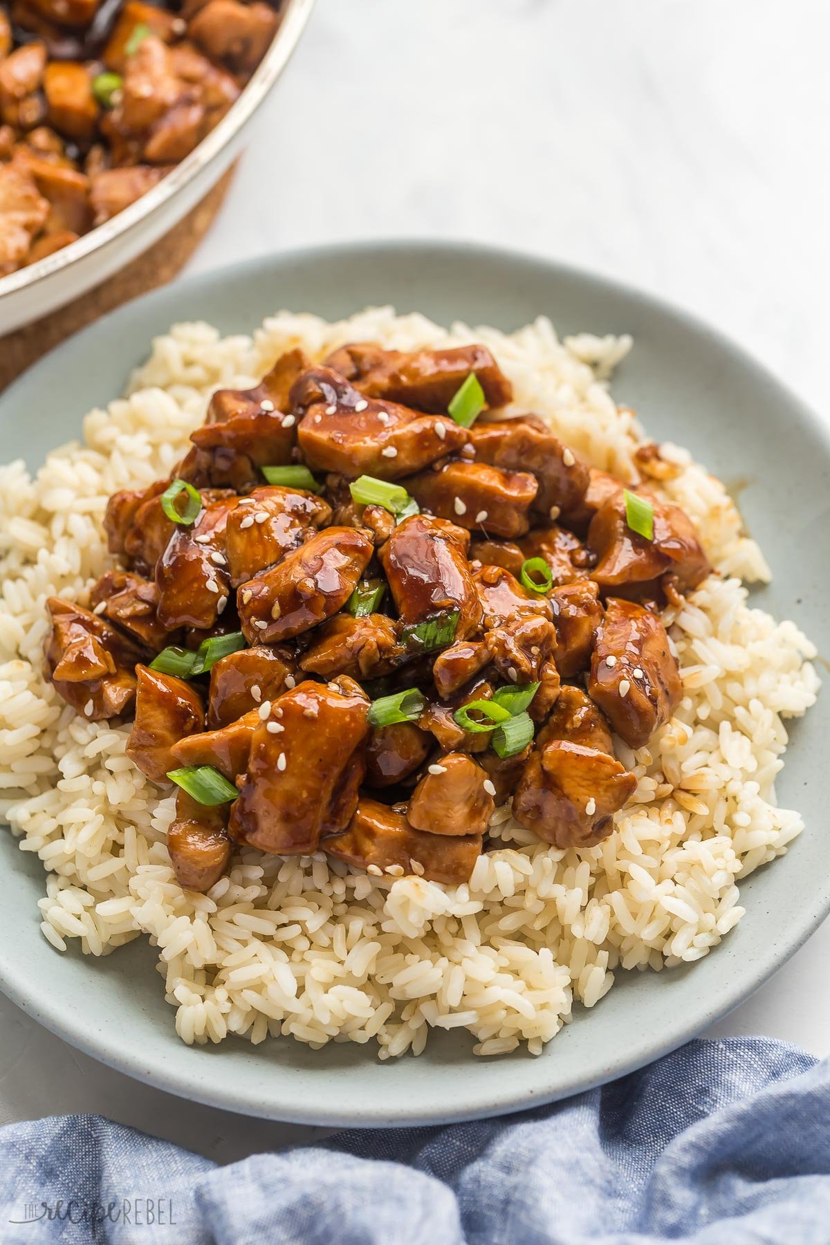 close up image of teriyaki chicken on a plate with green onions and sesame seeds.