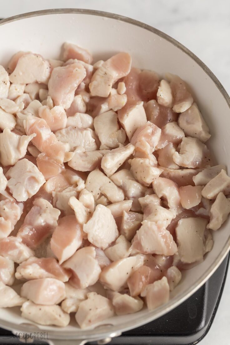 chunks of chicken breast cooking in white skillet