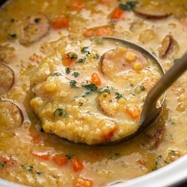 ladle scooping slow cooker lentil soup with kielbasa