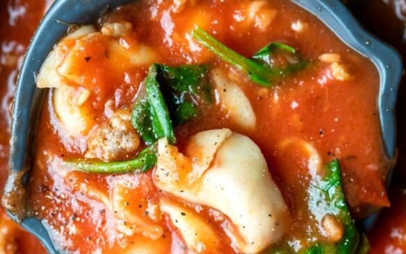 close up image of slow cooker tortellini soup in ladle