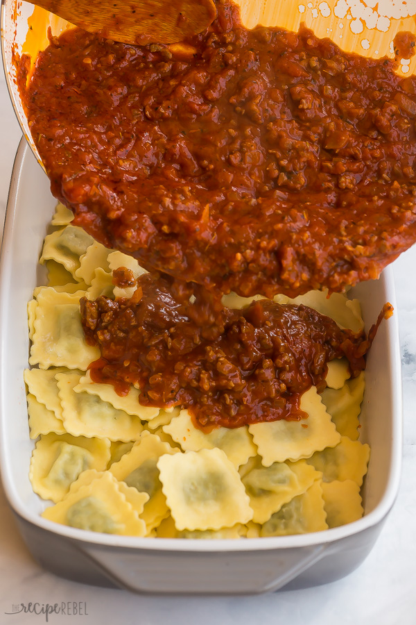 pouring meat sauce onto ravioli in pan