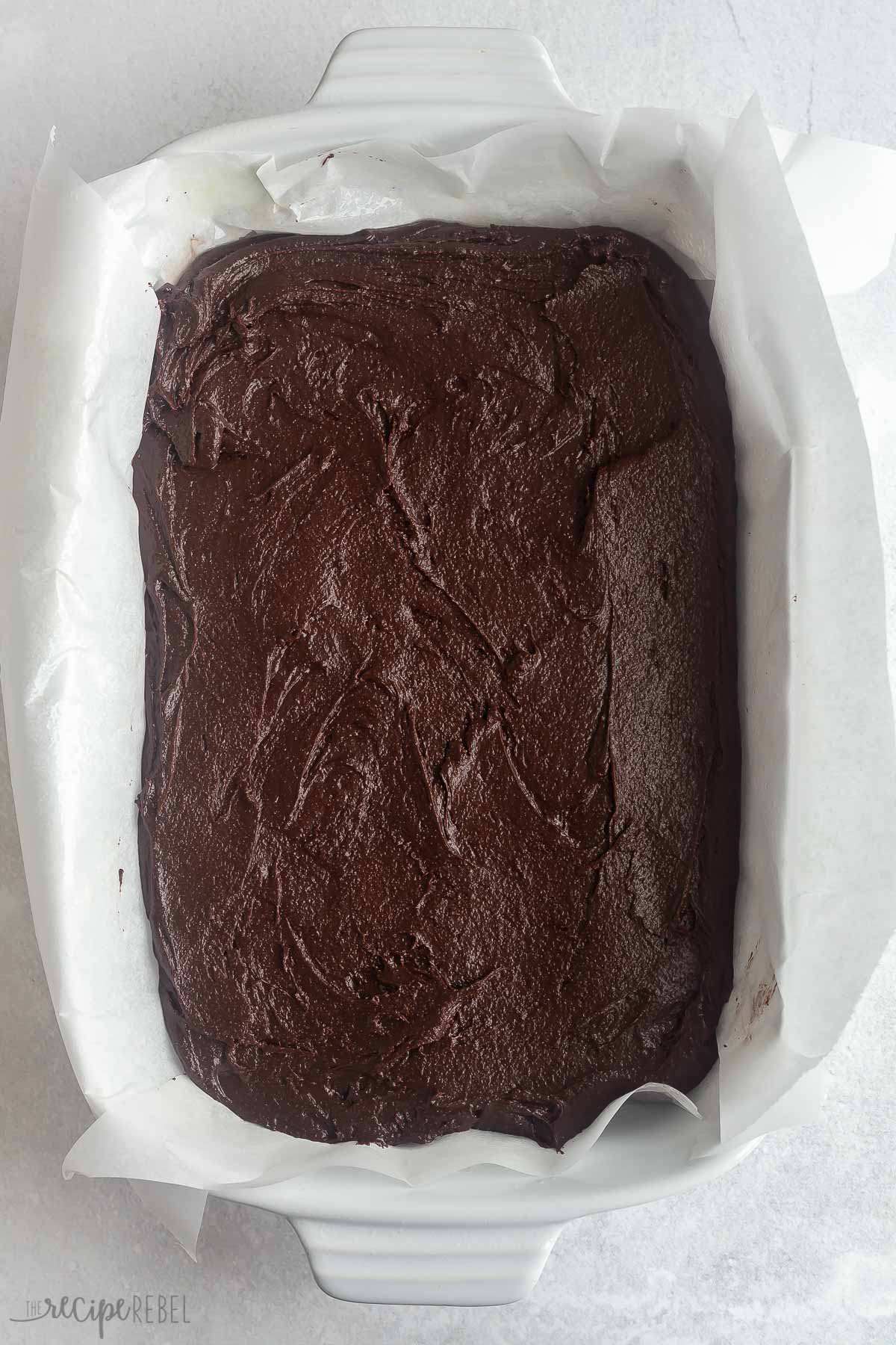 brownie batter spread into white baking dish lined with parchment paper.