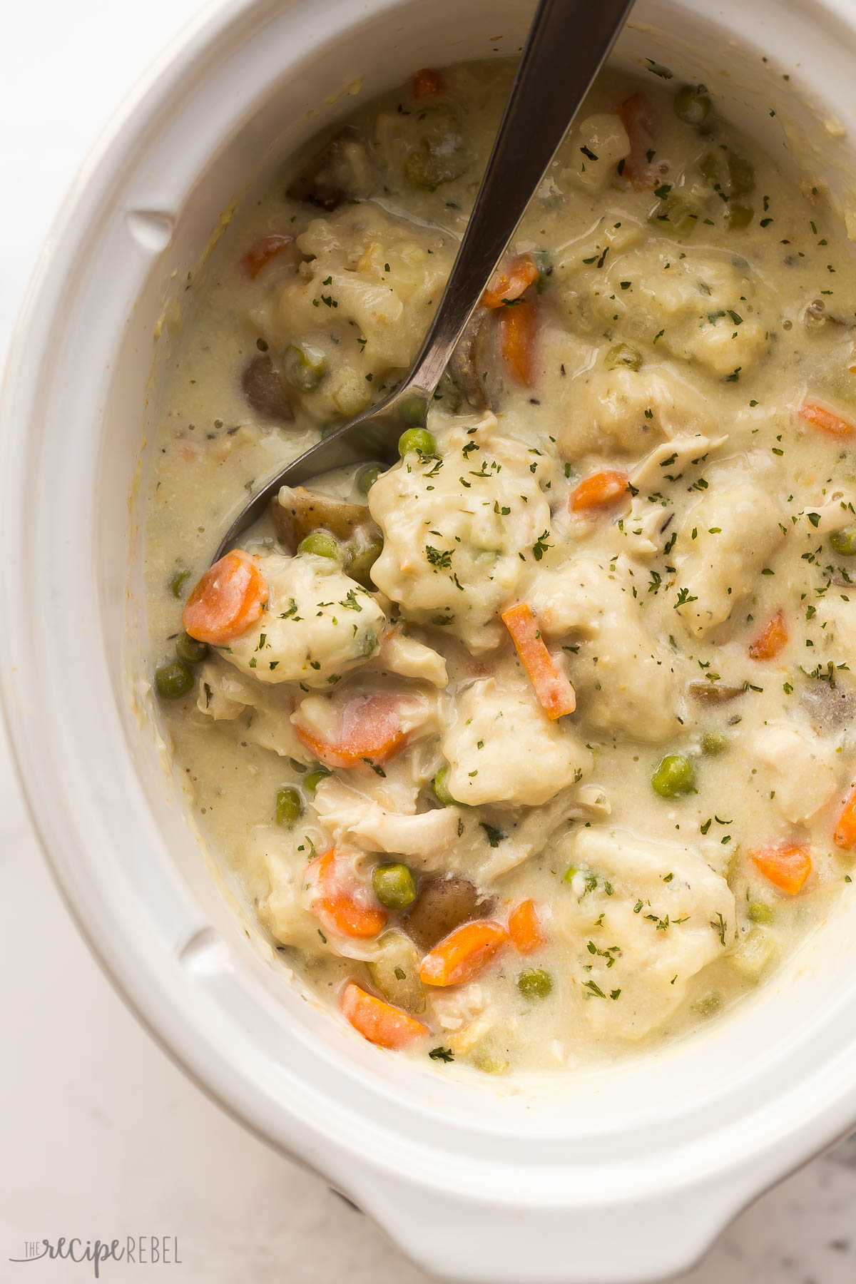 close up image of crockpot chicken and dumplings in white slow cooker with spoon