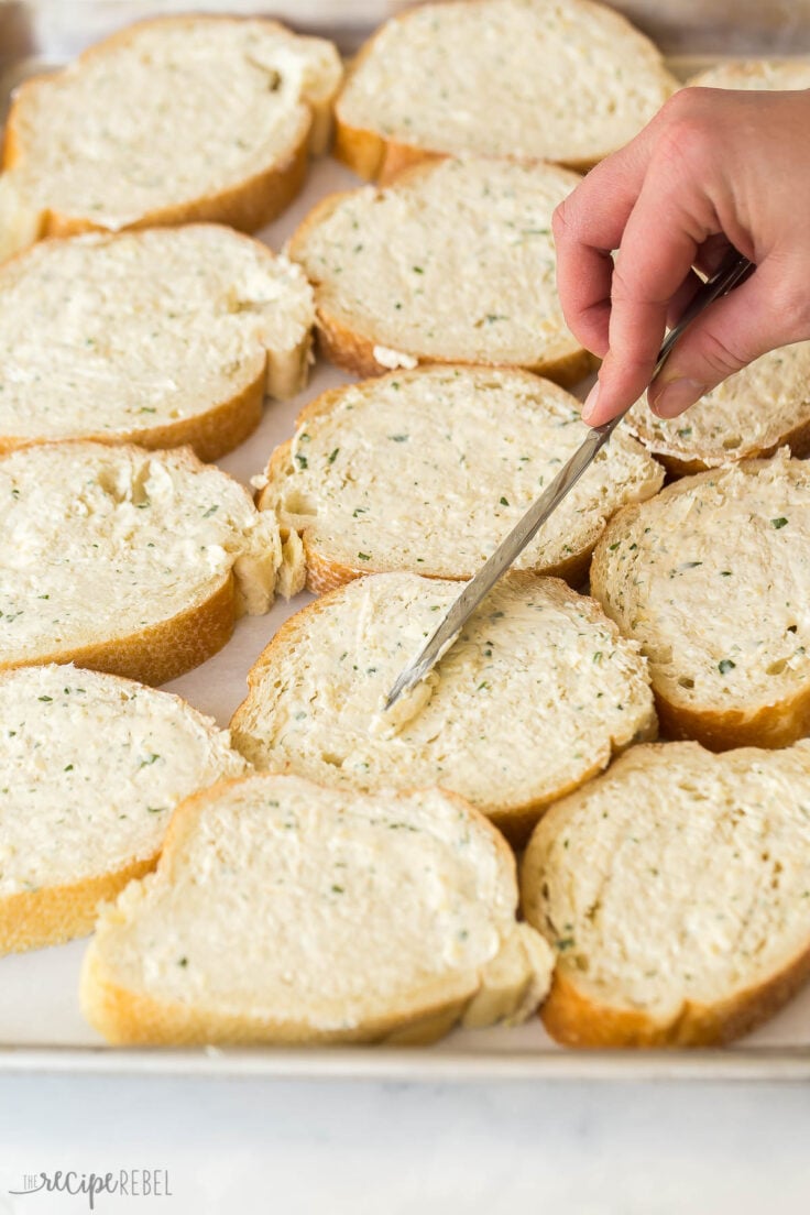 close up of knife spreading garlic butter on bread slices