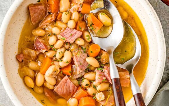 overhead image of bowl of ham and bean soup with two spoons