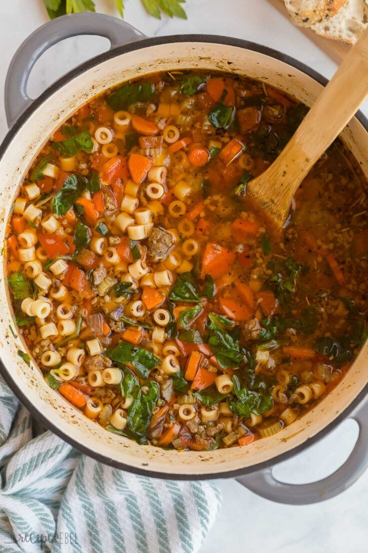 This Italian Sausage Soup is made in just one pot and takes 10 minutes to prep! It's an easy dinner that's loaded with flavorful Italian sausage, tons of veggies, perfectly cooked noodles, and parmesan cheese! #soup #recipe #dinner | easy soup recipes | italian sausage recipes | healthy soup recipes | noodle soup | easy dinner recipes overhead image of italian sausage soup in dutch oven with wooden spoon