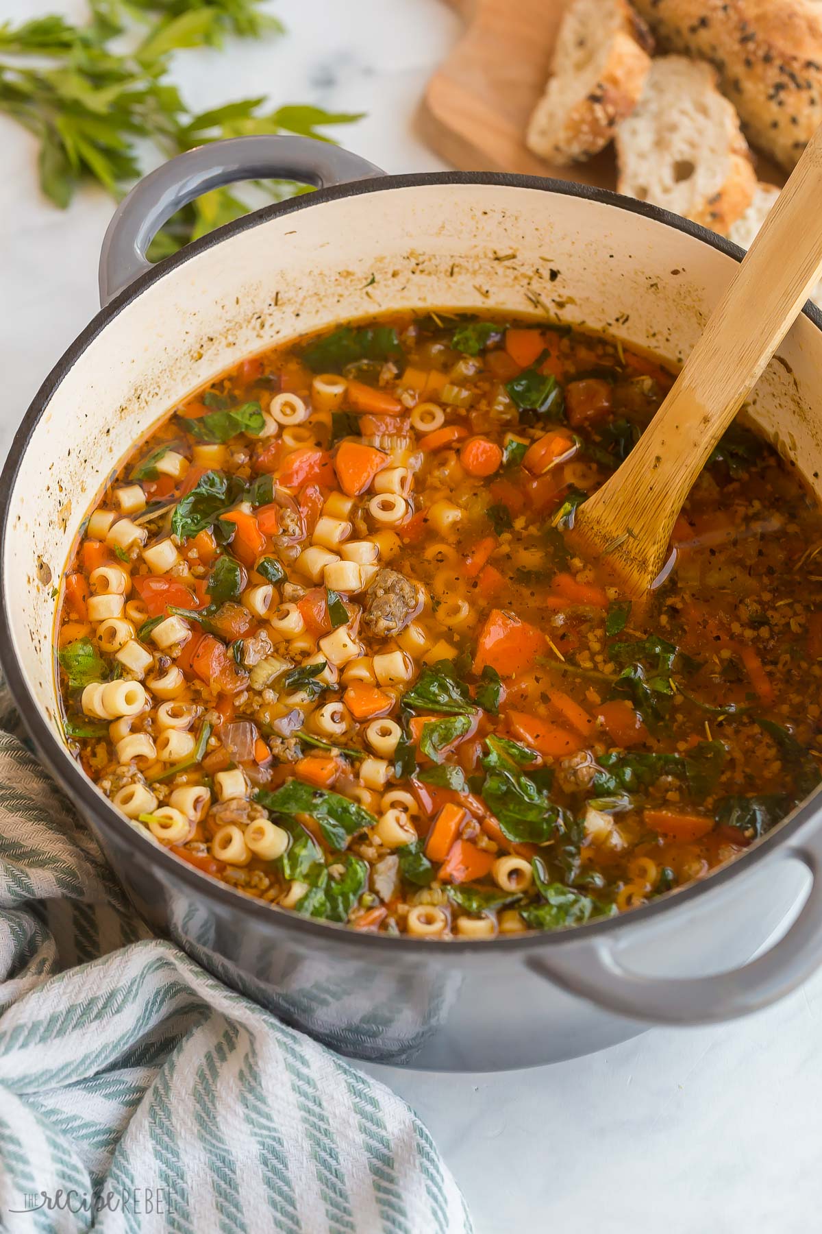 close up image of italian sausage soup in dutch oven with wooden spoon stuck in