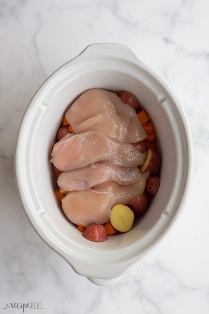 uncooked chicken breasts on top of vegetables in crockpot