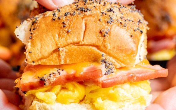 two hands holding ham egg and cheese breakfast sliders