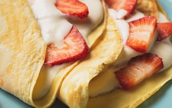 close up image of crepes with cream and strawberries