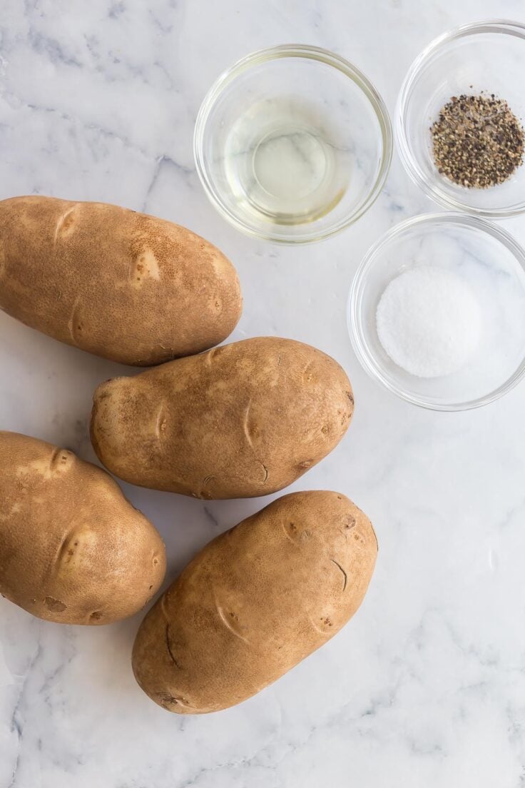 four russet potatoes with bowls of oil salt and pepper