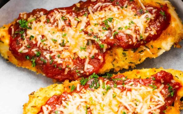 two pieces of air fryer chicken parmesan in air fryer basket on parchment paper