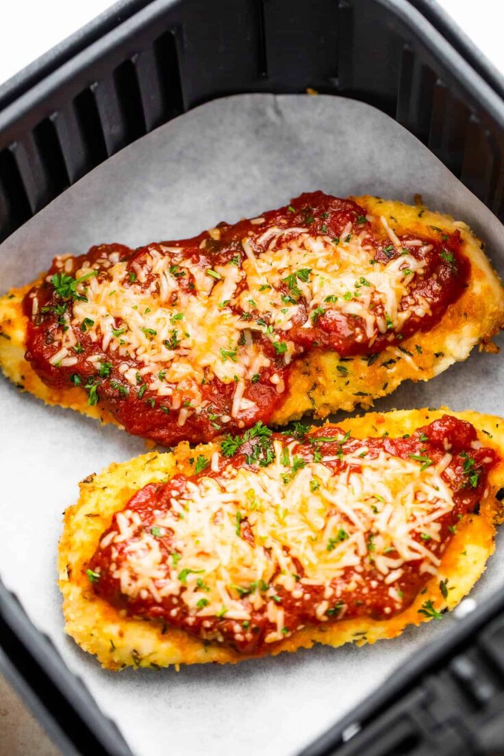 two pieces of air fryer chicken parmesan in air fryer basket on parchment paper