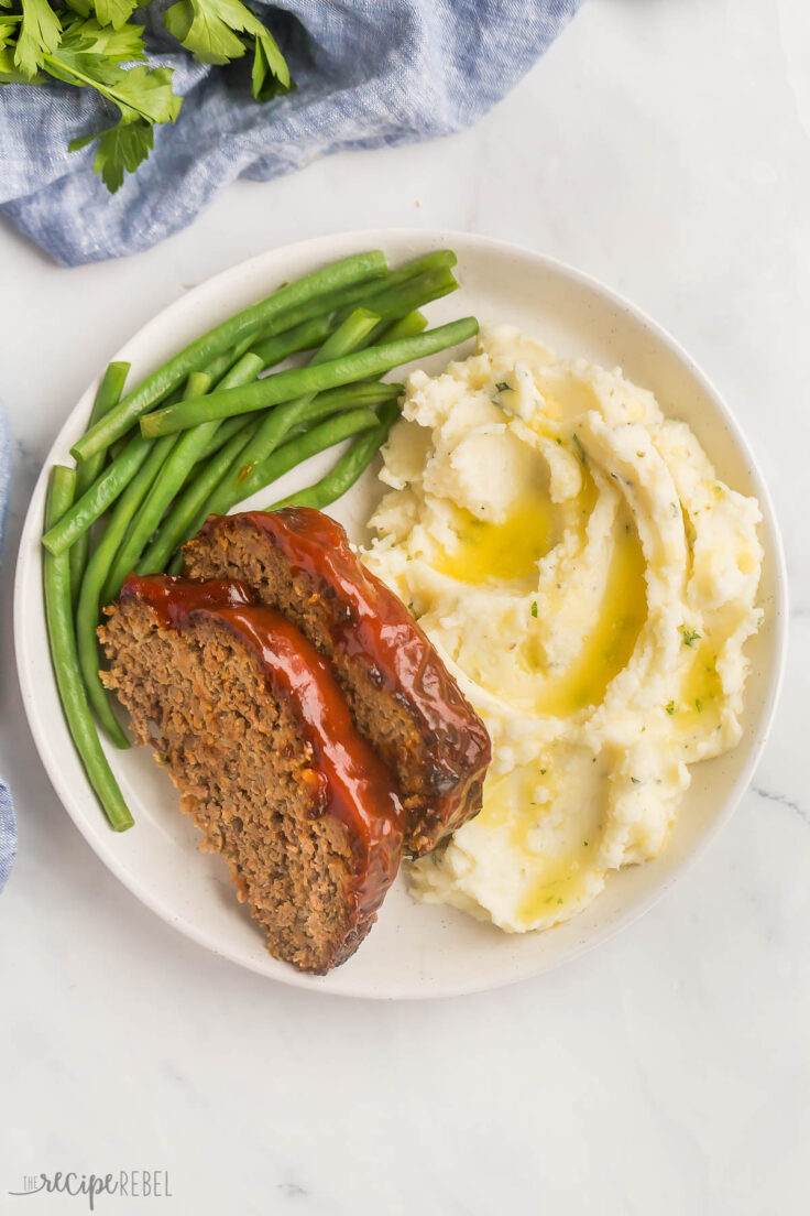 This Air Fryer Meatloaf is classic comfort food made quicker and easier in the air fryer! It's moist, tender, and juicy in the middle, with a slightly crispy exterior. #airfryer #dinner #recipes | air fryer recipes | air fryer dinner | ground beef recipes | easy dinner recipes | overhead image of two slices of air fryer meatloaf on mashed potatoes