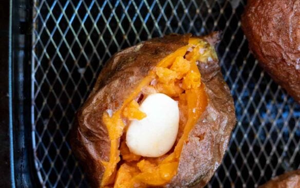 overhead image of sweet potato cut open in air fryer basket with butter