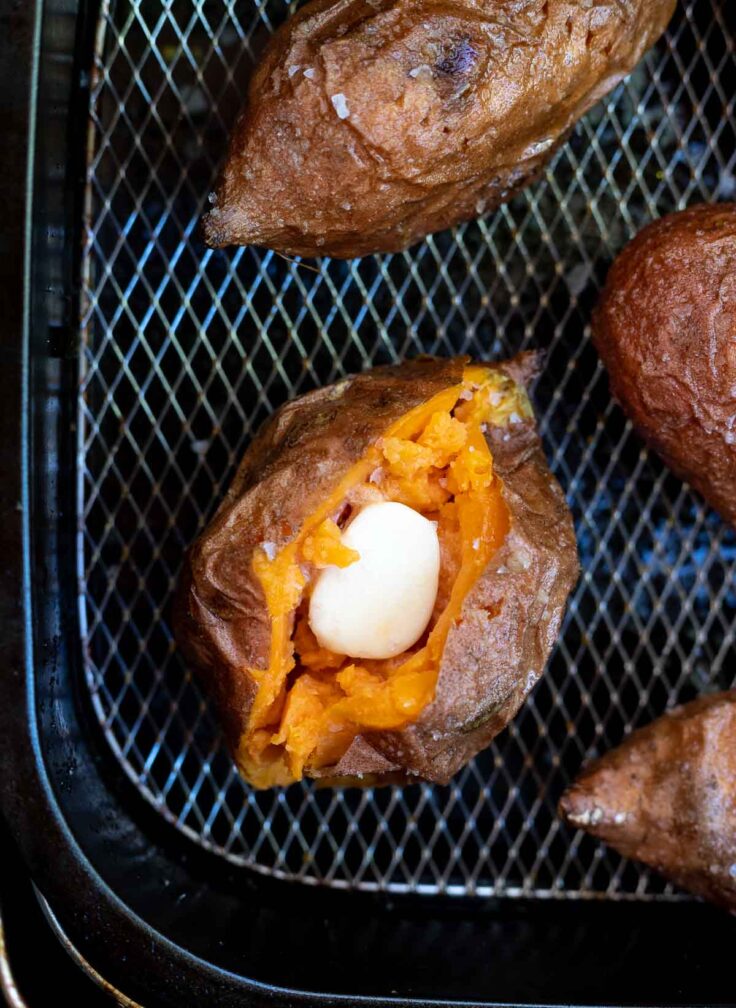 overhead image of sweet potato cut open in air fryer basket with butter