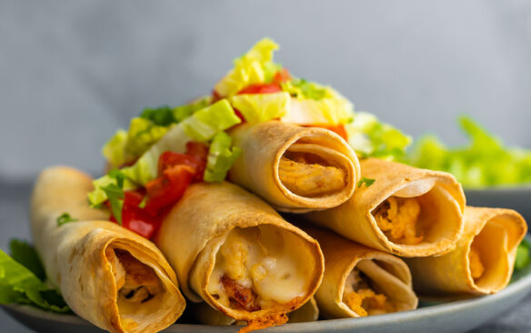 six air fryer chicken taquitos on a plate topped with lettuce and tomato