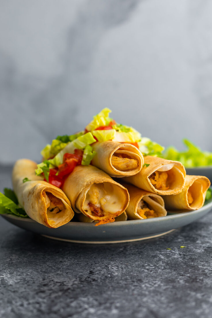 six air fryer chicken taquitos on a plate topped with lettuce and tomato